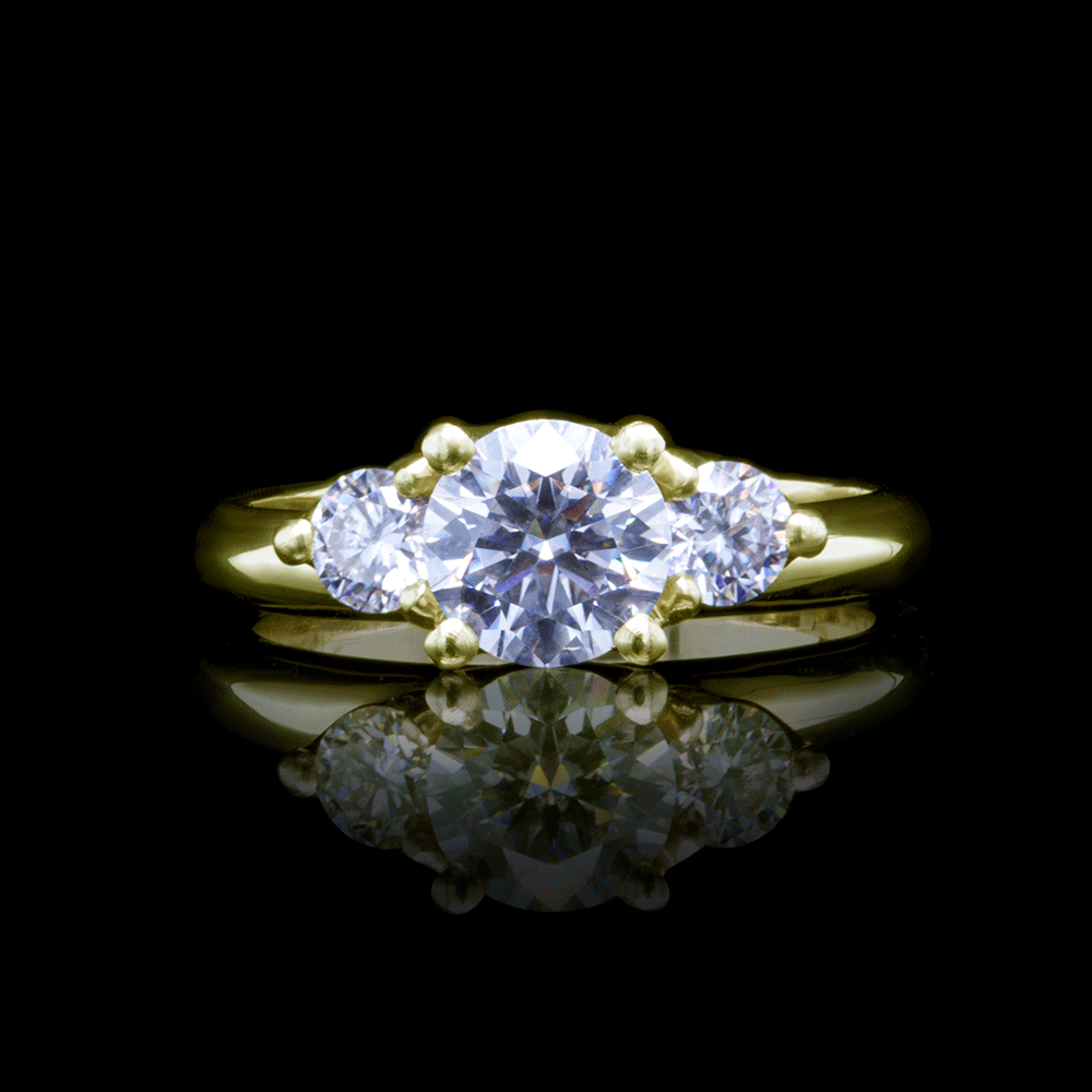 Three-stone moissanite engagement ring in yellow gold with dramatic black background reflection, highlighting the ring's architectural design and the stones' brilliance