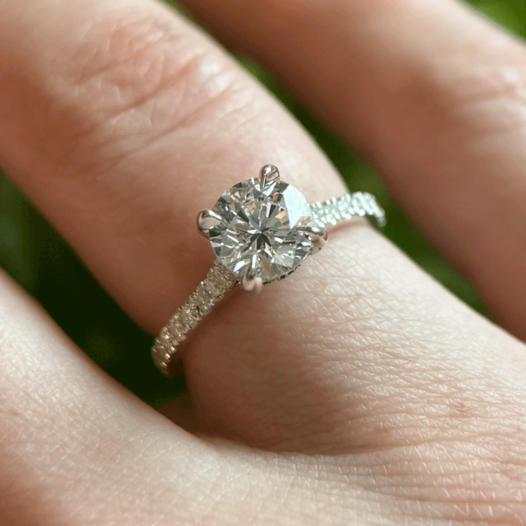 a close-up of a hand wearing a solitaire engagement ring. The ring features a prominent, possibly diamond, center stone set in a simple band. 