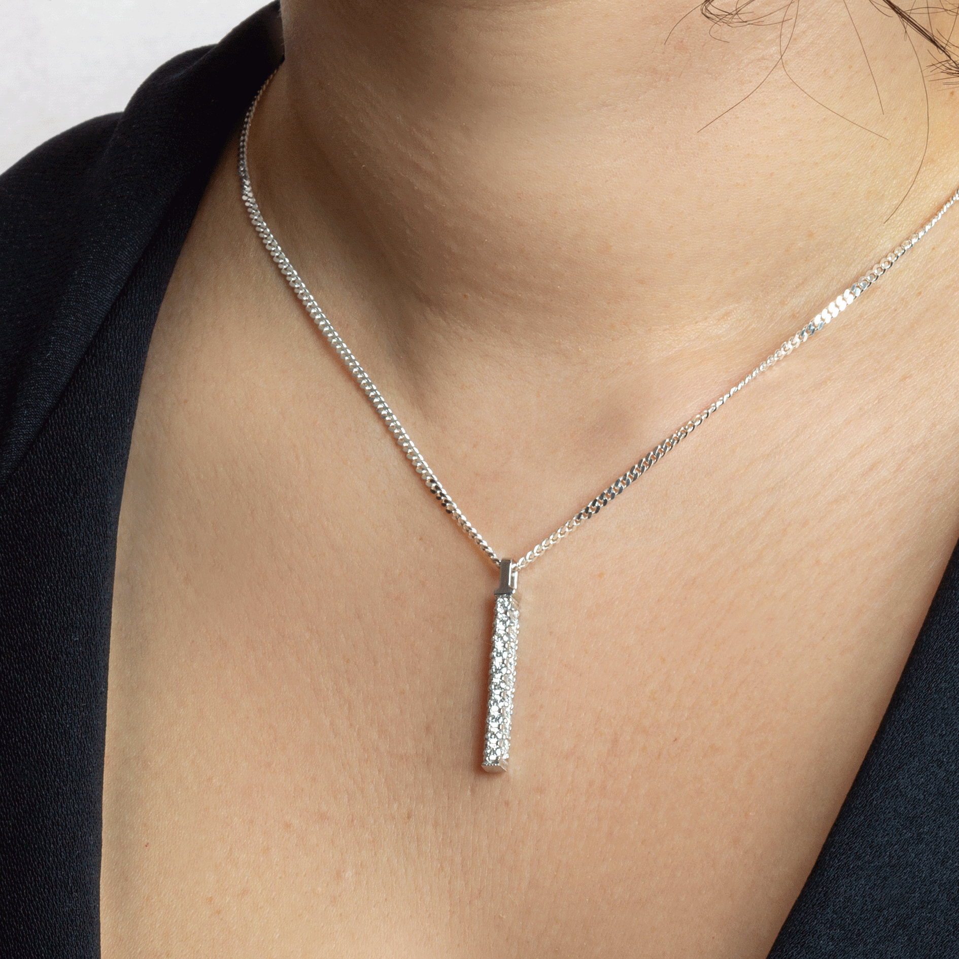 A simple, elegant necklace featuring a long, slender pendant. The pendant appears to be a vertical bar or rod, possibly with small embellishments or stones. The necklace is delicate and understated. 