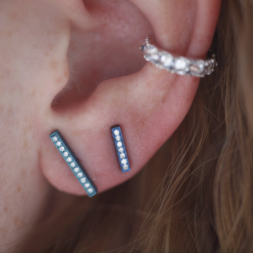 Showcasing two small, linear earrings and a slightly larger, curved earring that appears to be a huggie-style earring. The earrings have small, sparkly accents, possibly tiny gemstones or cubic zirconia.