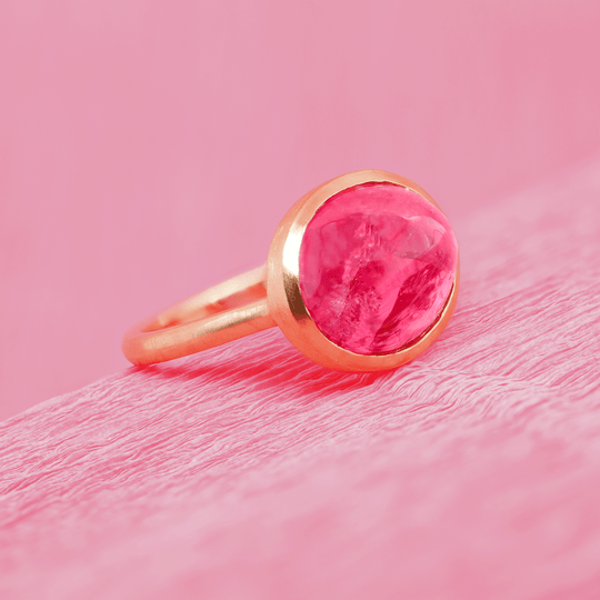 18k yellow gold ruby cabochon solitaire ring, side view. Sitting on pink paper