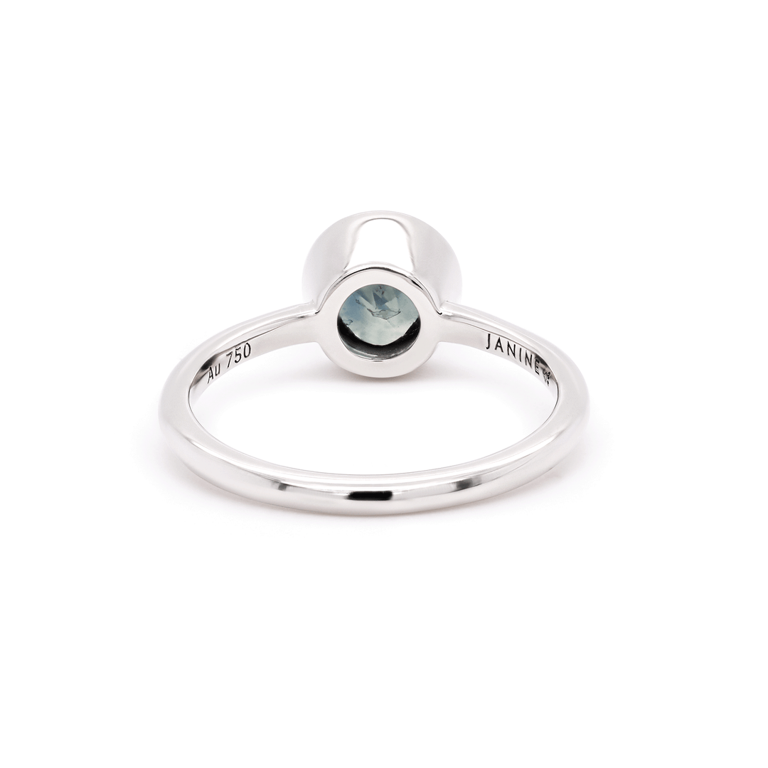 Single round blue sapphire solitaire ring set in gleaming 18K recycled white gold, photographed on a clean white background. Back view of ring.