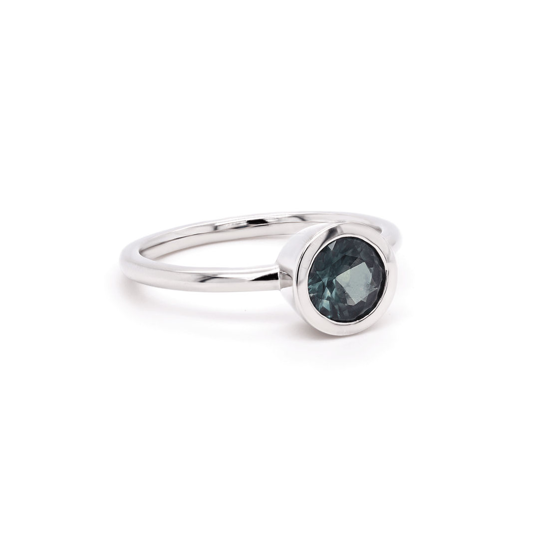 Single round blue sapphire solitaire ring set in gleaming 18K recycled white gold, photographed on a clean white background. Side view