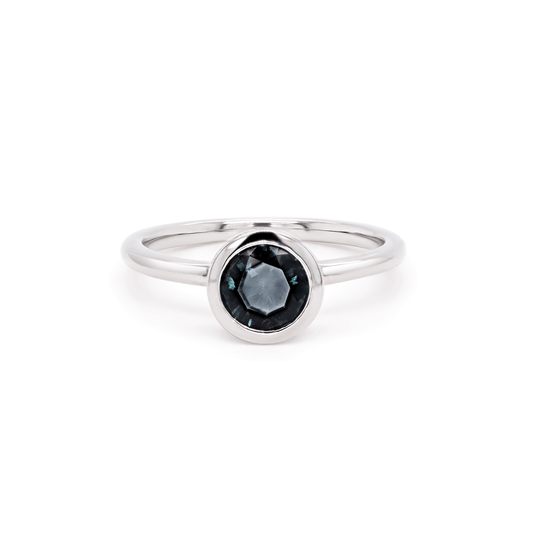 Single round blue sapphire solitaire ring set in gleaming 18K recycled white gold, photographed on a clean white background. Front view