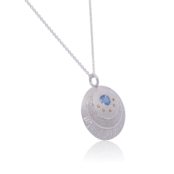 Artistic Luna Pendant necklace with hand-textured silver disc, moon motif, and blue topaz centre stone, on silver chain.