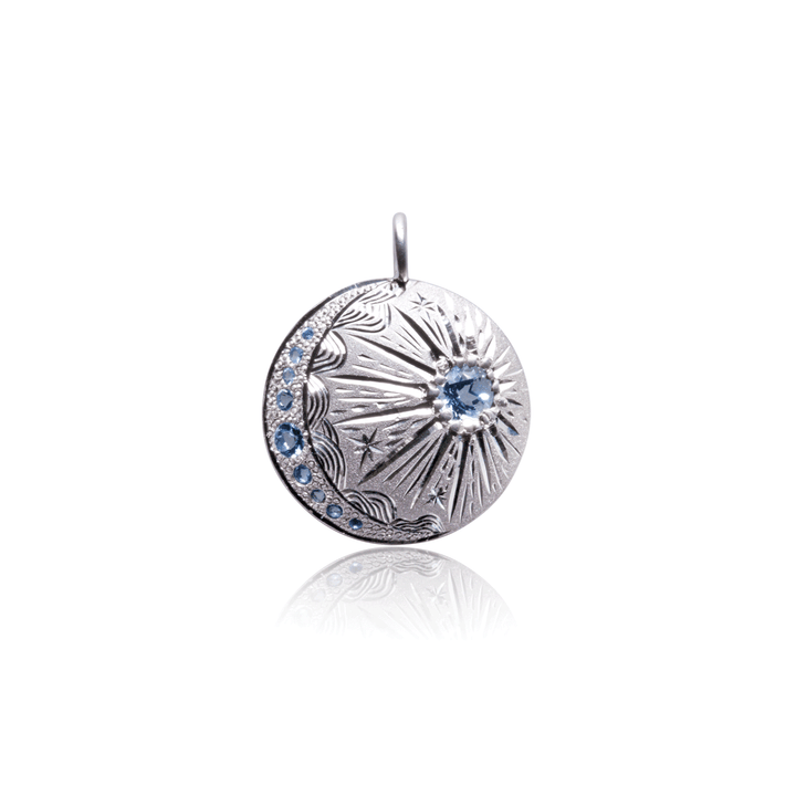 Sterling silver celestial charm pendant with hand-engraved starburst and blue topaz gems, artisanal design by Janine Jewels.