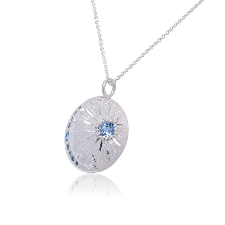 Janine Jewels handcrafted silver pendant necklace with radiant starburst motif and bezel-set blue topaz, celestial-inspired design.