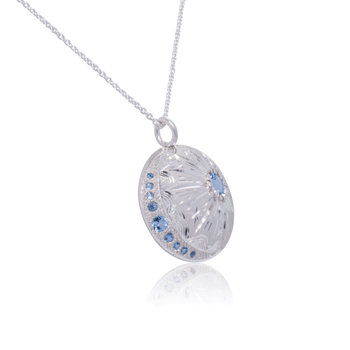 Lunar-inspired pendant necklace in sterling silver, featuring celestial engravings, graduated blue topaz stones, and fine silver chain.