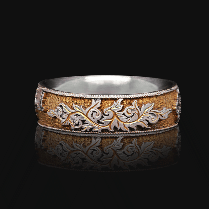 Front view of Gilded Gate ring in gold anodized titanium, showing detailed hand-engraved scroll motif, on a black background.