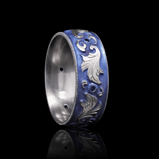 Angled view of blue anodized titanium ring with hand-engraved scroll design and sapphire accents, set against a black background.