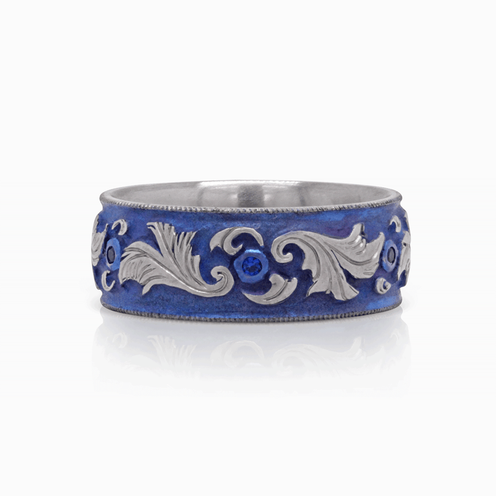 Front view of Lagoon Lustre titanium ring, showcasing blue anodized scroll design with bezel-set blue sapphires, on a white background.