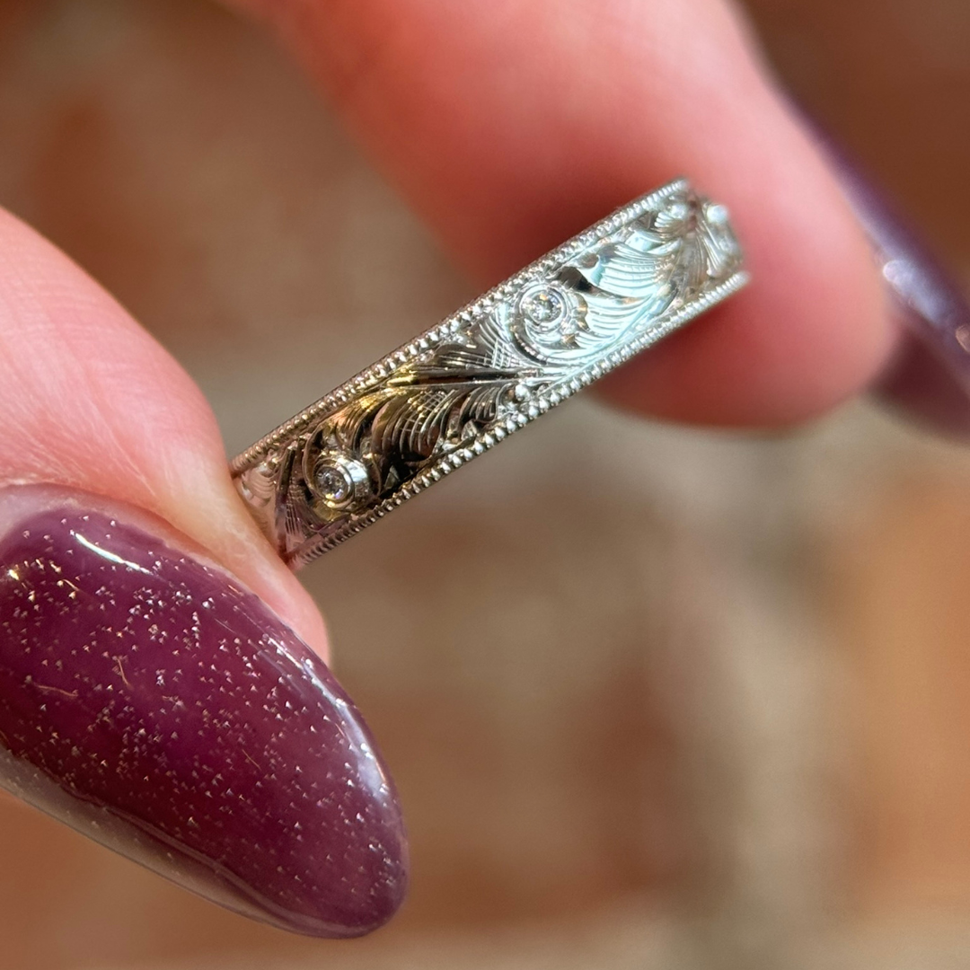 Close-up of a custom hand-engraved platinum wedding band with floral scrollwork, featuring delicate diamonds set along the band.